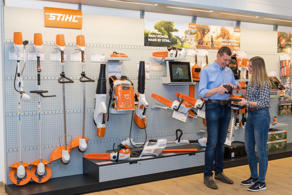 Staff member helping a customer with a Stihl hedge trimmer in the showroom, with Stihl trimmers, blowers and saws on display